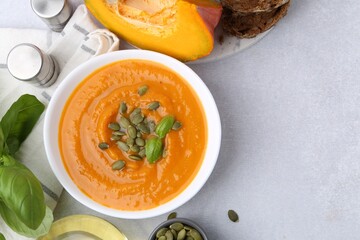 Delicious pumpkin soup with seeds and basil in bowl served on light table, flat lay. Space for text