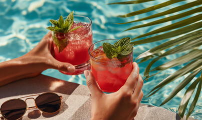 Warm sunshine highlights hands holding colorful summer drinks near a sparkling pool Generative AI