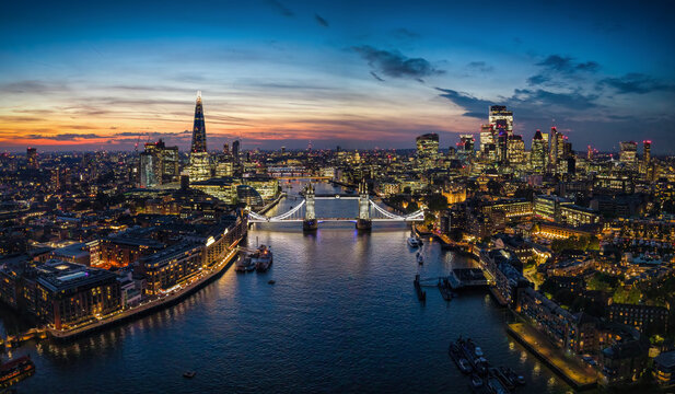 Wide, panoramic evening view of the illuminated skyline of London, United Kingdom, with Thames river, Tower Bridge and City skyscrapers