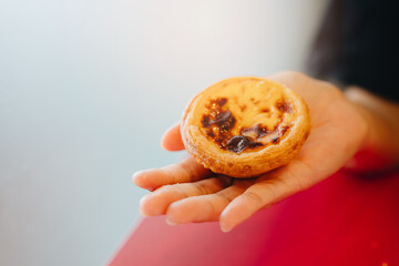 Dessert concept. Hand Holding a Freshly Baked Creamy Custard Dessert with a Golden Brown Crust on a Red Table