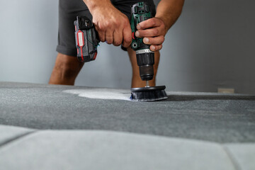 Man cleaning sofa upholstery using drill brush attachment