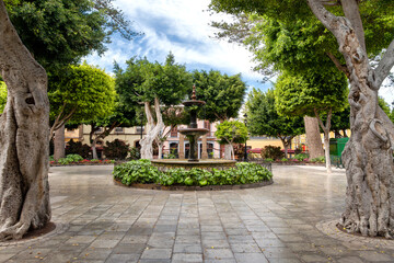 Gáldar, Canary Islands – Village square Plaza de Santiago with traditional fountain, mature trees and peaceful greenery.