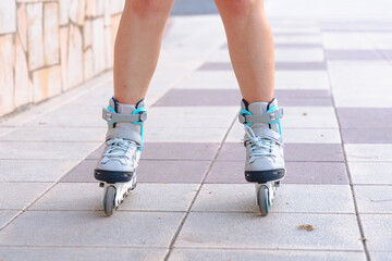 Detailed close-up of young woman wearing roller skates on pavement, focusing on her legs and...