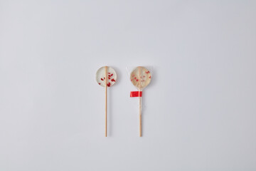 Two artisanal clear lollipops with dried red fruit pieces, one wrapped and one unwrapped, isolated on a clean white background.