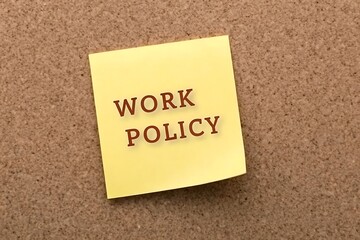 Yellow sticky note with the words work policy written in black text on a cork board background
