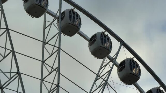 A panoramic, wide-angle, low-angle shot captures the top half of a massive, modern white Ferris wheel in a dramatic silhouette against a dark, stormy, overcast sky with patches of bright light and