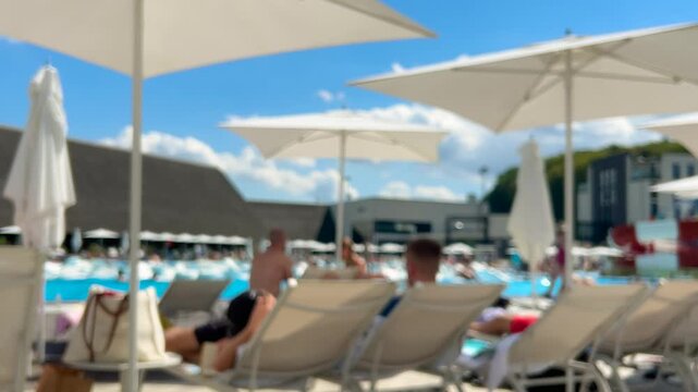 Relaxation area by the pool with plenty of sun loungers and parasols. Out of focus.