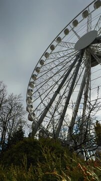 A striking low-angle, wide-view shot of a modern, large white Ferris wheel, its intricate metal structure and passenger cabins dominating the upper right frame. The scene is set against a bright