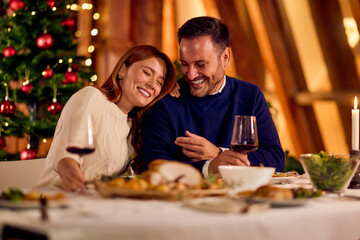 Happy Couple Enjoying New Year Dinner By Christmas Tree With Wine And Candles