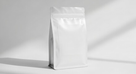 A blank, white coffee bag stands upright with a shadow cast on a plain background.