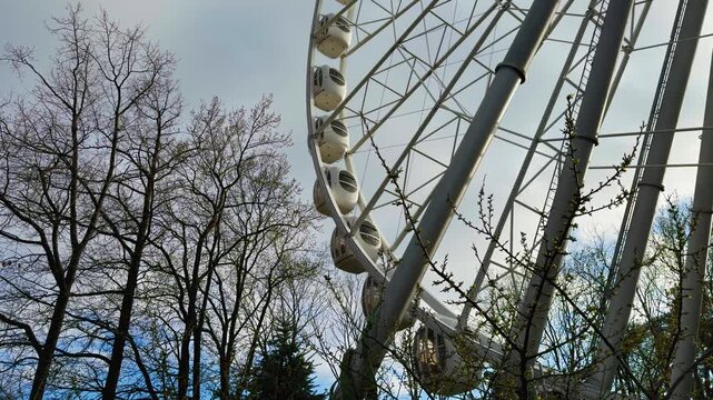 A striking low-angle, wide-view shot of a modern, large white Ferris wheel, its intricate metal structure and passenger cabins dominating the upper right frame. The scene is set against a bright
