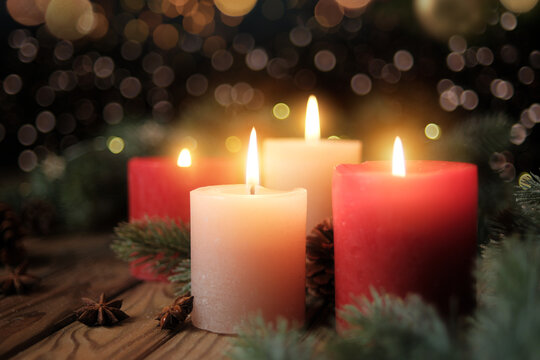 Four burning candles with dark blurred background. Tranquil Christmas mood with Advent candleflames, fir branches and lights
