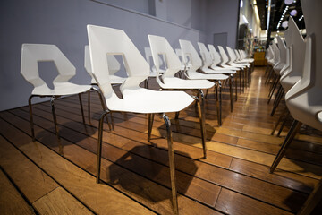 Modern white chairs arranged in a row on a polished wooden floor, ready for a professional event or presentation