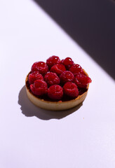 Round tartlet with large raspberries on top on a white background