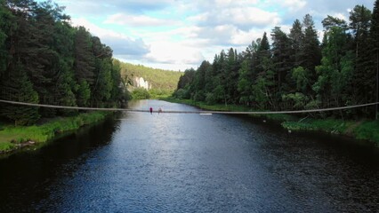 Fototapeta premium Tourists relaxing on rope bridge over scenic river