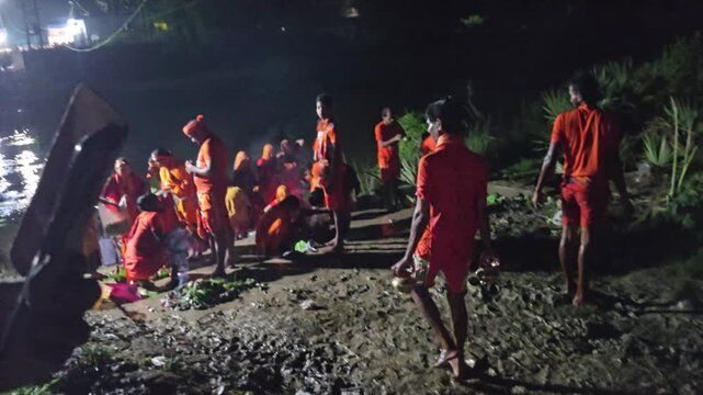 Authentic documentary footage of Kanwariya devotees gathering at a riverbank during the sacred Kanwar Yatra in India. Wearing traditional saffron clothing and carrying decorated Kanwars