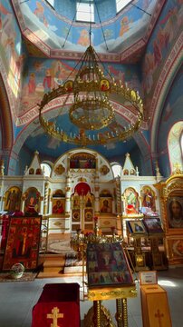 A striking low-angle, wide-view shot capturing the richly decorated interior of a modern Orthodox Church. The scene is dominated by a massive golden chandelier suspended beneath the central dome
