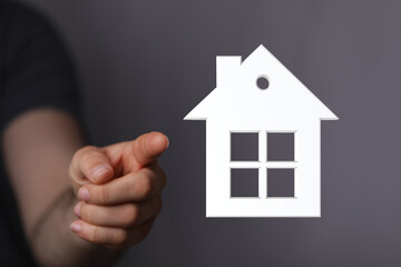 A hand points to a 3D white house symbol, representing real estate, home ownership, and the concept of buying a house. Conceptual image for prop