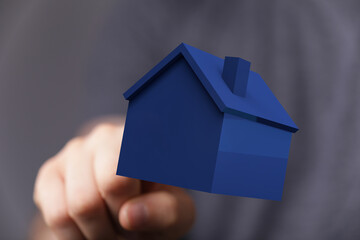 Hand pointing towards a blue 3D house model, symbolizing home, real estate, ownership, and dream....