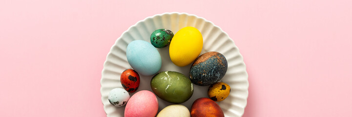 A collection of vibrant Easter eggs in various colors is artfully arranged on a white plate, set against a soft pink background, capturing the essence of the holiday's decorations, banner