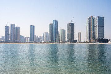 Fototapeta premium Modern skyscrapers along turquoise waterfront in sunny day, urban coastal view. 