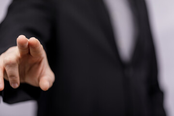Close up of a hand gesturing a direction with two fingers towards the viewer. A man in a black suit...