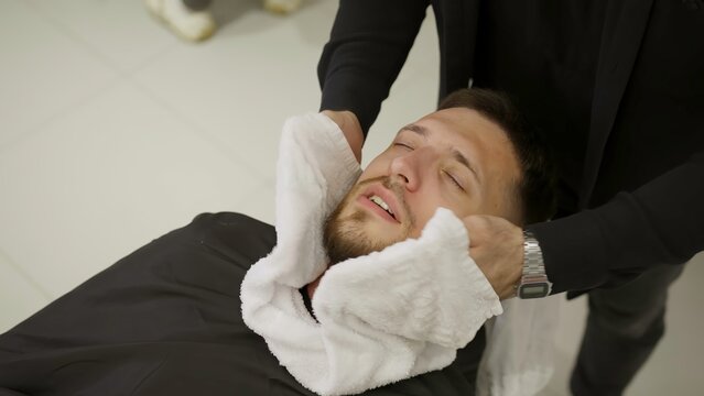 Barber wrapping man's face with hot towel. Clip - Powered by Adobe