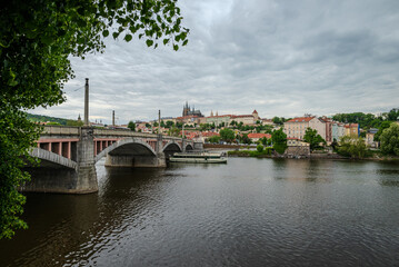 Manes Bridge over the Vltava River in Prague, Czech Republic, under soft May clouds, with a distant view of Prague Castle