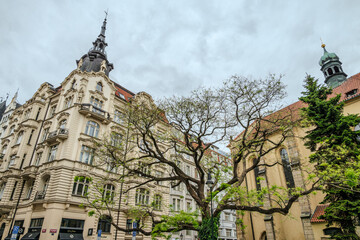 Attractive buildings with Bohemian architecture in Prague Old Town, Czech Republic, under rainy May clouds with a tree of fresh spring leaves in the foreground