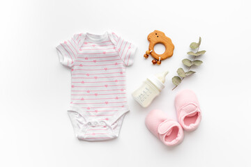 Baby bodysuits and eco friendly accessories - booties, wooden rattle toy and baby bottle with milk on white background, top view