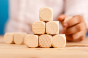 Person building a pyramid structure with wooden blocks. Concept of building, strategy, and teamwork. Perfect for illustrating concepts of succes