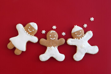 Smiling gingerbread family on a red background with snowflakes around, copy space for text. Christmas time