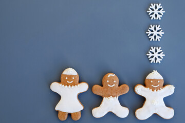Smiling gingerbread family on a blue background with snowflakes, copy space for text. Christmas time