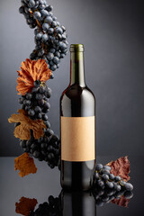 Bottle of red wine with blue grapes on a black reflective background.