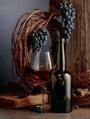 An antique bottle of port wine against the backdrop of an old weathered board, dried vine, and blue grapes.