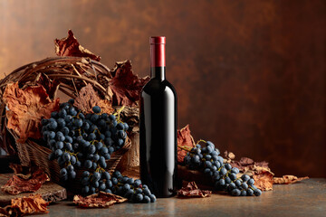 Bottle of red wine with blue grapes on a brown background.