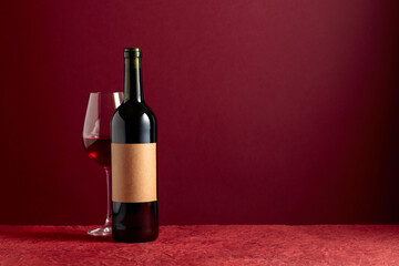 Bottle with old empty label and glass of red wine on a red background.