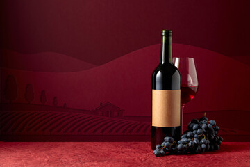 Bottle and glass of red wine with blue grapes on a red background.