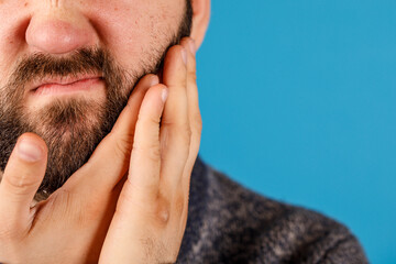 Obraz premium Close-up of a man holding his face, possibly in pain, with a blue background. Perfect for health, wellness, or discomfort themes.