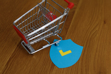 A shopping cart next to a blue verification badge on a wooden background, concept for online...