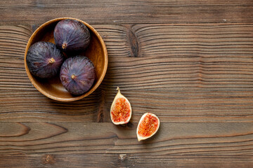 Purple ripe figs in a wooden bowl top view on a wooden background