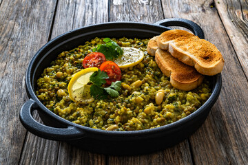 Green lentil and white bean stew with bread in cast iron pan on wooden table