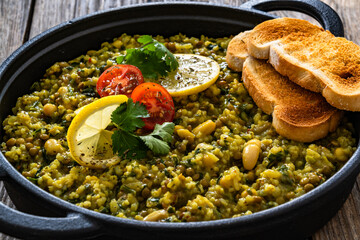 Green lentil and white bean stew with bread in cast iron pan on wooden table