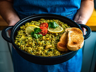 Woman holding pan with green lentil and white bean stew with bread, close-up