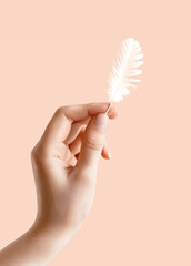 A beautiful hand of yuong girl with feather isolated pink background. A mockup for designers