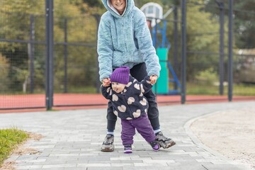 Baby learning to walk with parent outdoors. Development milestones