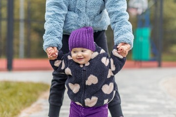 Baby walking with adult's help outside. Development milestones