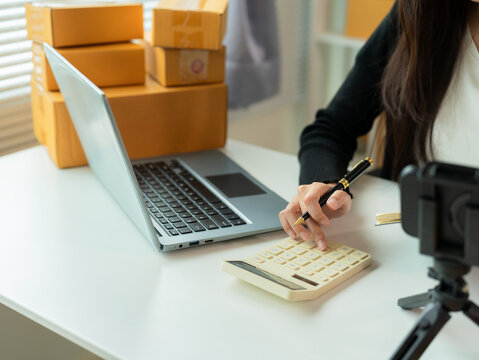 Asian SME businesswoman working in home office, checking customer orders on online marketplace, preparing to box and sell to customers, SME business idea, close up. - Powered by Adobe