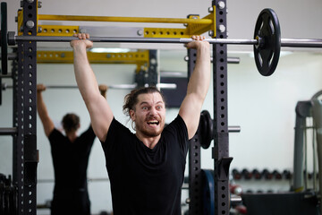 Young man intense effort during overhead press in gym