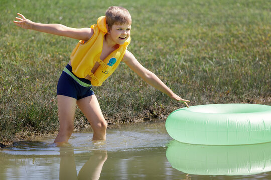 A cheerful boy plays with his green inflatable lifebuoy in the water on a hot summer day
